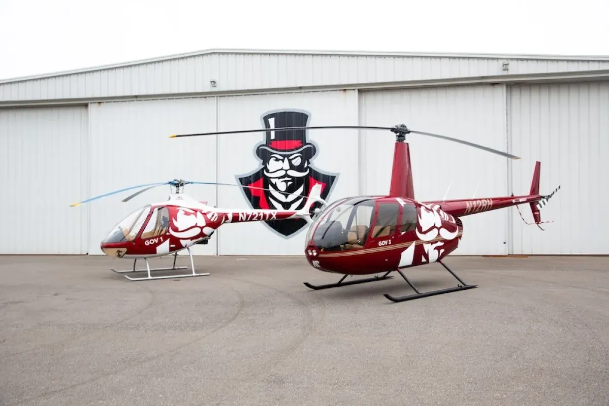 Two red Austin Peay training helicopters parked outside a hangar with the Governors logo
